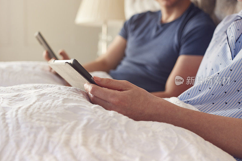 在Covid - 19封锁期间，一对夫妇在家躺在床上使用数字平板电脑和手机